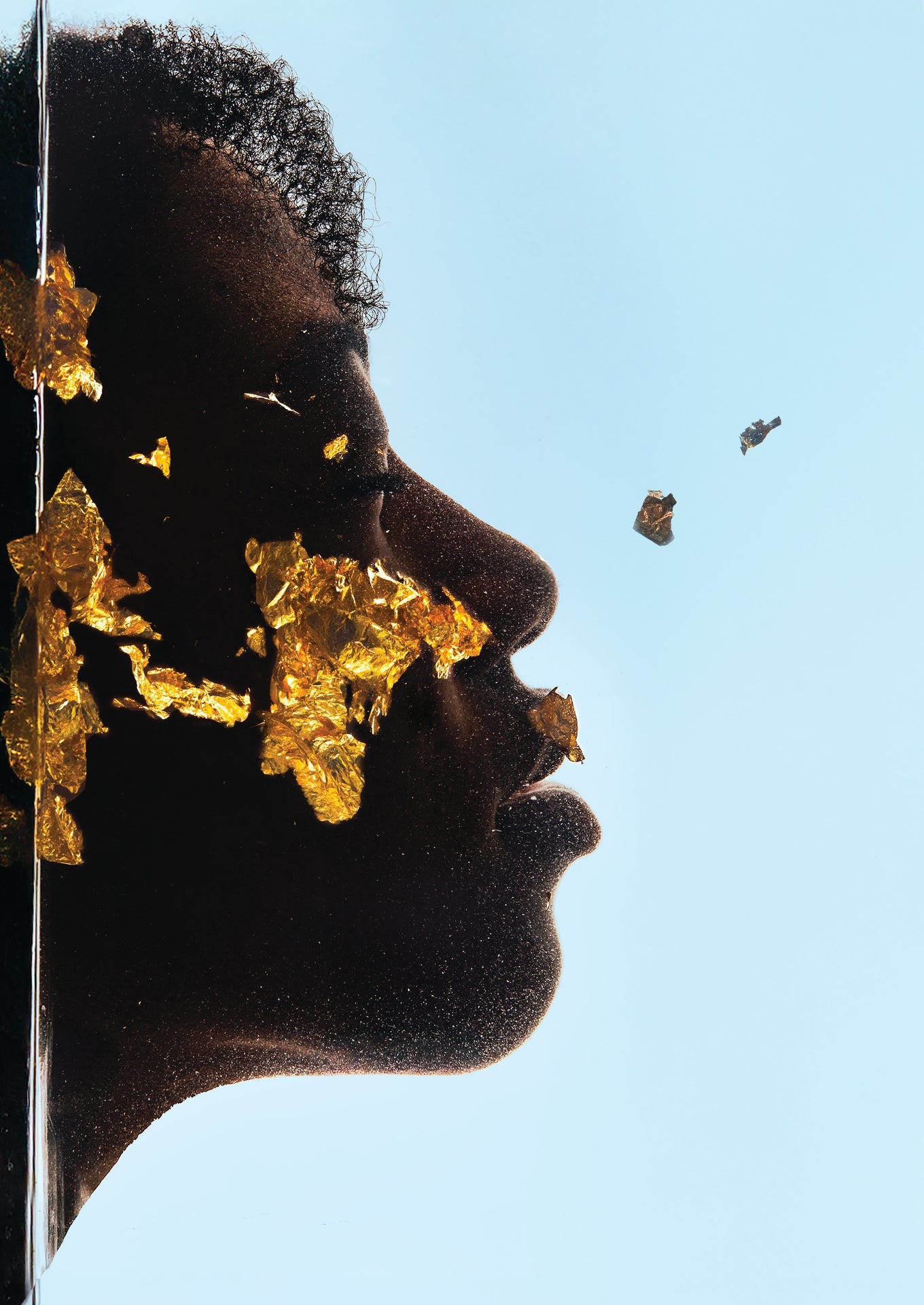 Close-up of a person's face with gold leaf on their hair against a blue sky.